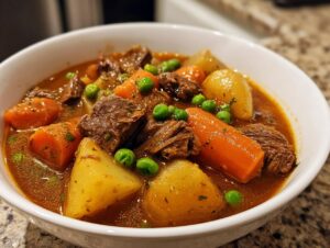 Close-up of a rich, savory bowl of vegetable beef soup featuring chunks of beef, carrots, potatoes, and bright green peas.