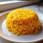 A perfectly molded mound of bright yellow turmeric rice served on a white plate, ready to eat.