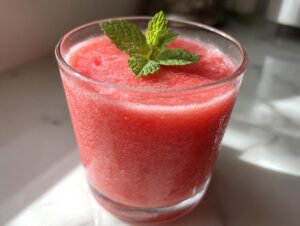 Close-up of a vibrant red watermelon smoothie in a glass, topped with fresh mint leaves.