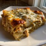 Close-up of a cheesy, layered serving of green chile chicken enchiladas topped with melted cheese and herbs.