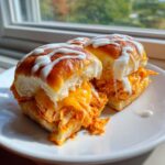 Two gooey buffalo chicken sliders on a white plate, drizzled with white ranch or blue cheese dressing.