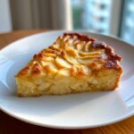 A close-up, appetizing slice of amazing apple tart featuring caramelized apple slices on a moist cake base, served on a white plate.