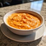Close-up of a thick, orange-colored beer cheese dip served in a white bowl on a saucer.