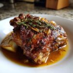 Close-up of a single serving of perfectly glazed braised chicken thighs topped with fresh thyme sprigs.