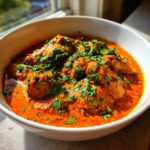 Close-up of tender chicken pieces swimming in a rich, orange-red sauce, garnished with fresh cilantro, a perfect butter chicken.