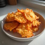 A close-up shot of a small bowl piled high with golden, crispy, homemade cheese crackers.