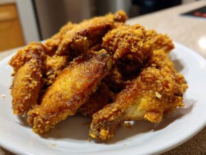 A close-up of a pile of golden brown, extra crunchy chicken wing pieces served on a white plate.
