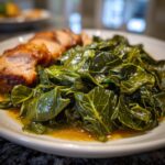 Close-up of tender, braised collard greens swimming in savory pot liquor next to sliced pork.