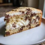 Close-up of a generous slice of cookie cake recipe filled with white cream and chocolate chips.