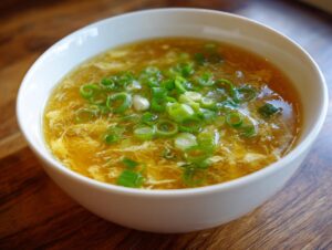 A white bowl filled with golden egg drop soup, garnished generously with fresh sliced green onions.