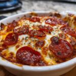 A close-up, appetizing shot of baked pepperoni pizza dip, bubbling with melted cheese and topped with herbs.
