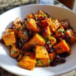 A close-up of vibrant orange cubes in a sweet potato salad mixed with dried cranberries and fresh parsley.