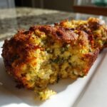 Close-up of a baked stuffing muffin, showing a crispy brown exterior and moist interior flecked with green herbs.