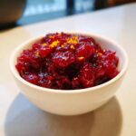 Close-up of glistening, chunky homemade cranberry sauce topped with bright orange zest in a white bowl.