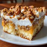 A moist slice of butter pecan praline poke cake topped with whipped cream and pecans.