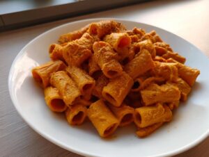 Close-up of rigatoni pasta coated thickly in bright orange butternut squash pasta sauce, seasoned with pepper.