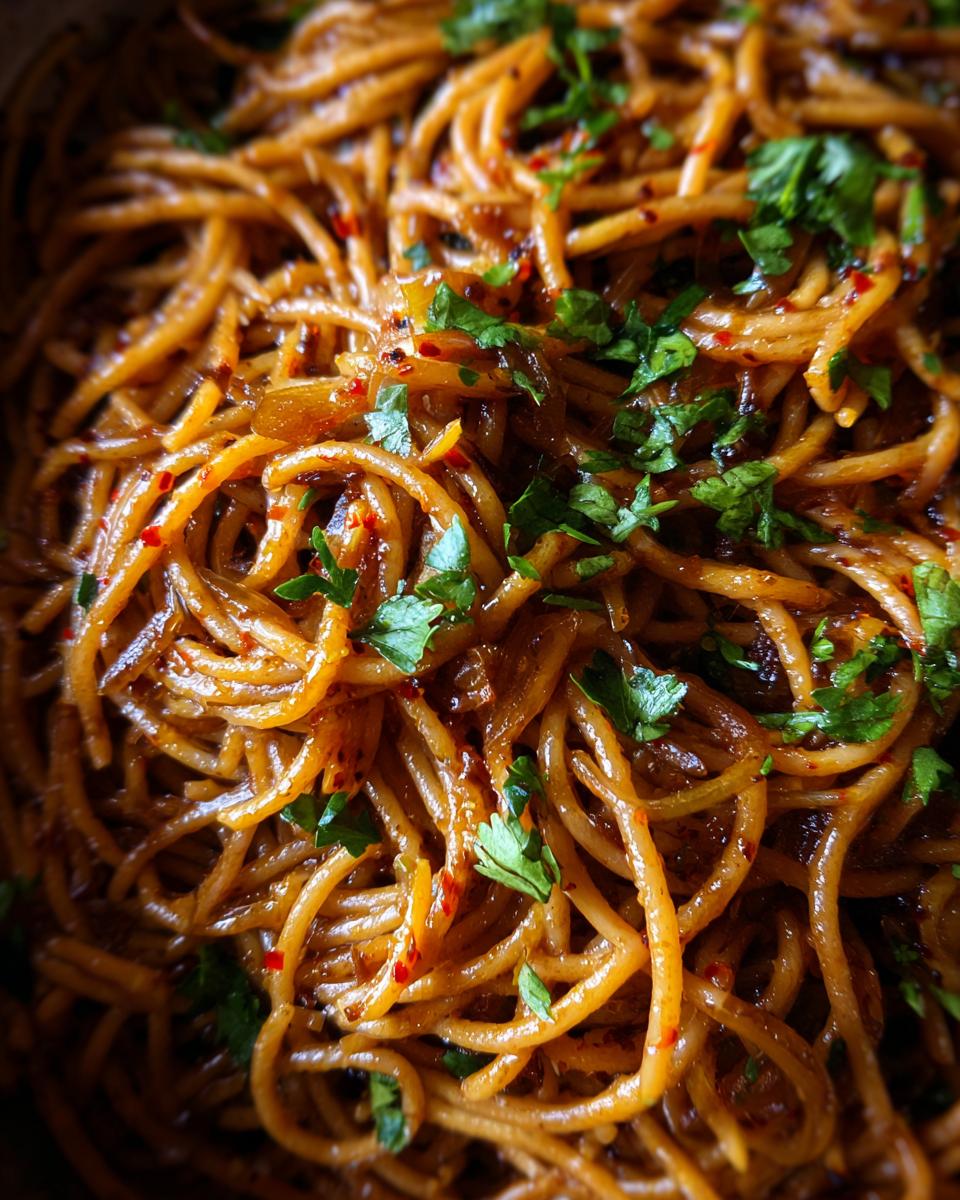 A close-up shot of glossy, brown spaghetti coated in sauce, featuring caramelized onions and fresh parsley, highlighting the caramelized onion pasta.