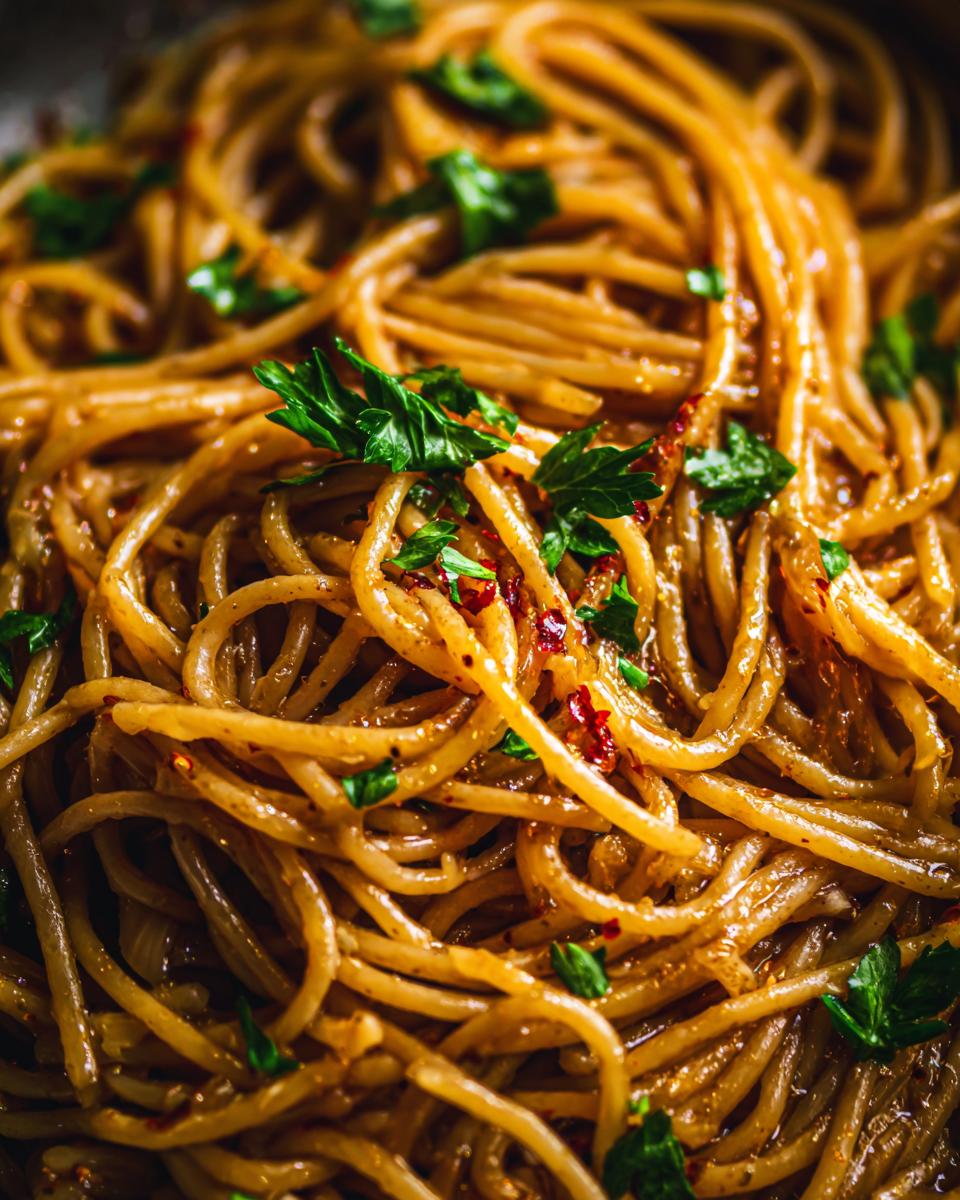 Close-up shot of glistening spaghetti tossed in a rich sauce, ready to serve, featuring caramelized onion pasta.