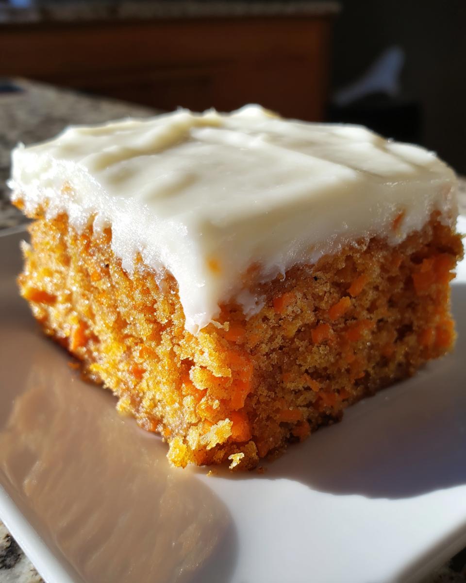 Close-up of a moist, square slice of carrot cake bars topped with thick cream cheese frosting.