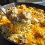 A spoonful of cheesy chicken and rice lifted from a skillet, showing melted cheese strings.