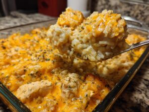 A spoonful of creamy, cheesy chicken and rice lifted from a glass baking dish topped with melted cheddar.