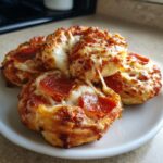 Four golden brown pizza pinwheels topped with melted cheese and pepperoni slices, showing a cheese pull.