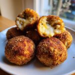 Close-up of golden fried rice balls, one is cut open revealing a gooey, melted cheesy center.