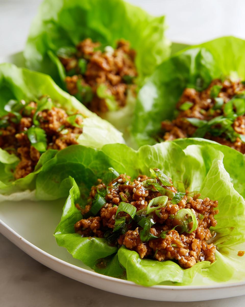 Four servings of savory chicken lettuce wraps filled with seasoned ground chicken and topped with green onions.