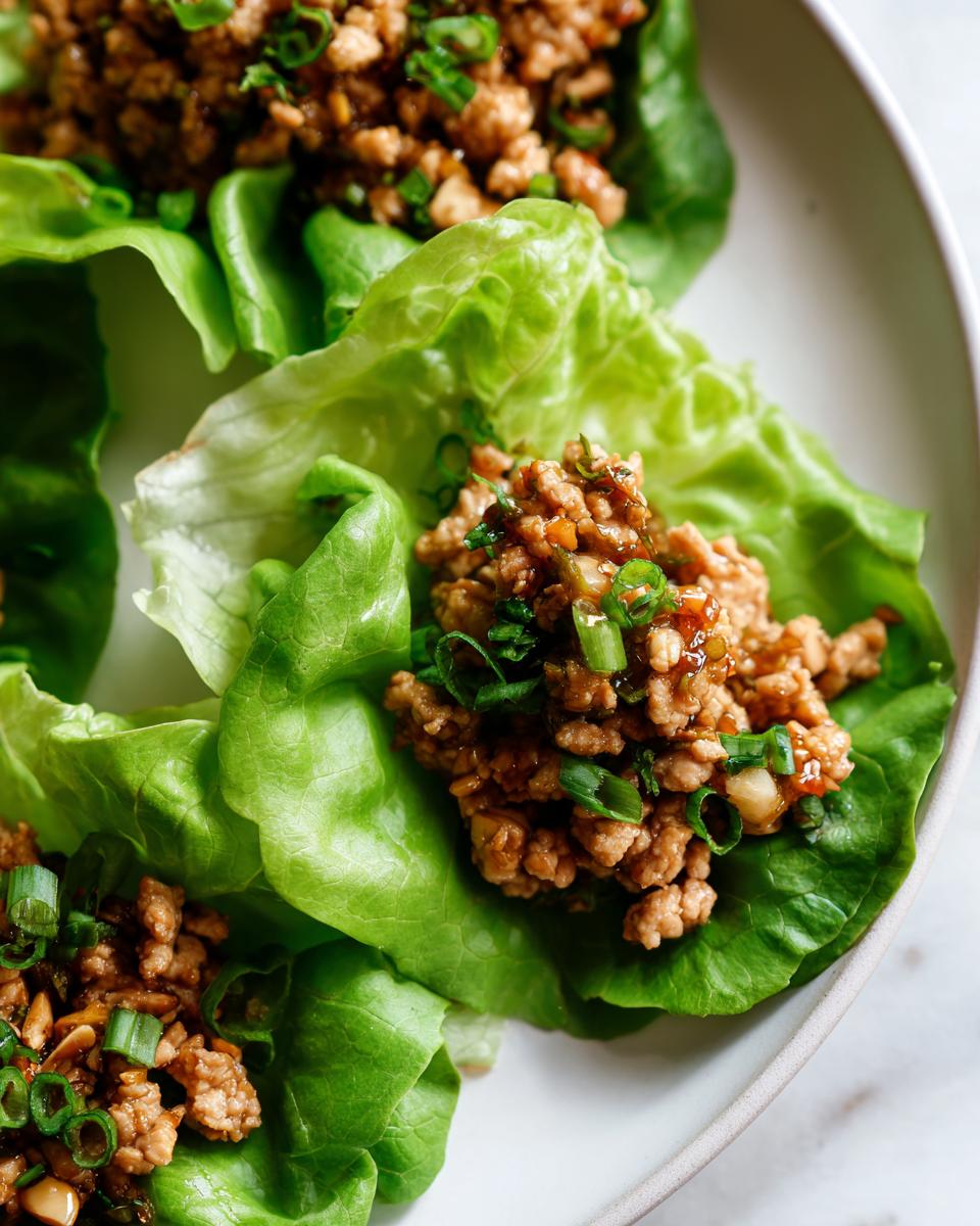 Close-up of three fresh chicken lettuce wraps filled with savory ground chicken mixture and topped with green onions.