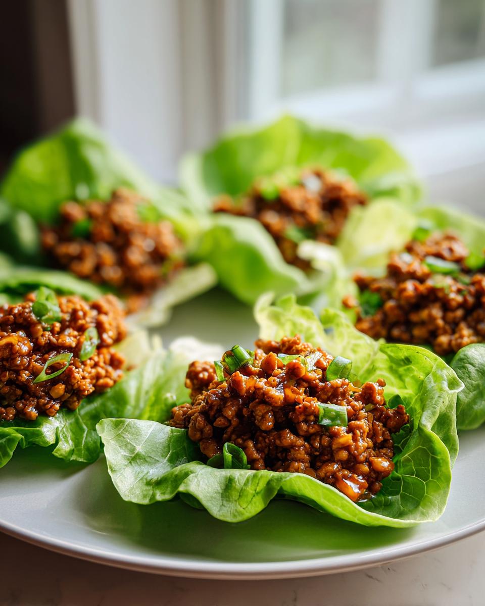 Close-up of several fresh chicken lettuce wraps filled with savory brown ground chicken mixture and topped with green onions.