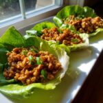 Three servings of savory chicken lettuce wraps filled with seasoned ground chicken and topped with green onions.