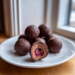 A plate of homemade chocolate covered cherries, one cut open revealing the cherry center.