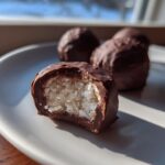 A close-up of a chocolate covered coconut balls treat, showing the shredded white coconut filling inside.
