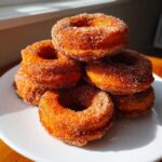 A close-up stack of moist baked pumpkin donuts coated generously in cinnamon sugar.