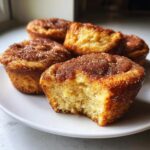 Close-up of fluffy cinnamon sugar french toast muffins on a white plate, one muffin has a bite taken out.