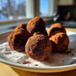 A close-up of several rich, cocoa-dusted oreo balls resting on white parchment paper on a plate.