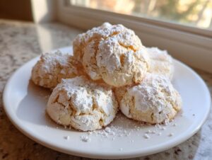 A stack of soft, crinkle-top cool whip cookies heavily dusted with powdered sugar on a white plate.