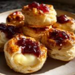 Close-up of golden, flaky cranberry brie bites with melted brie cheese oozing out and topped with dark red jam.