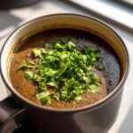 Close-up of a dark, creamy black bean soup topped generously with bright green chopped cilantro or parsley.