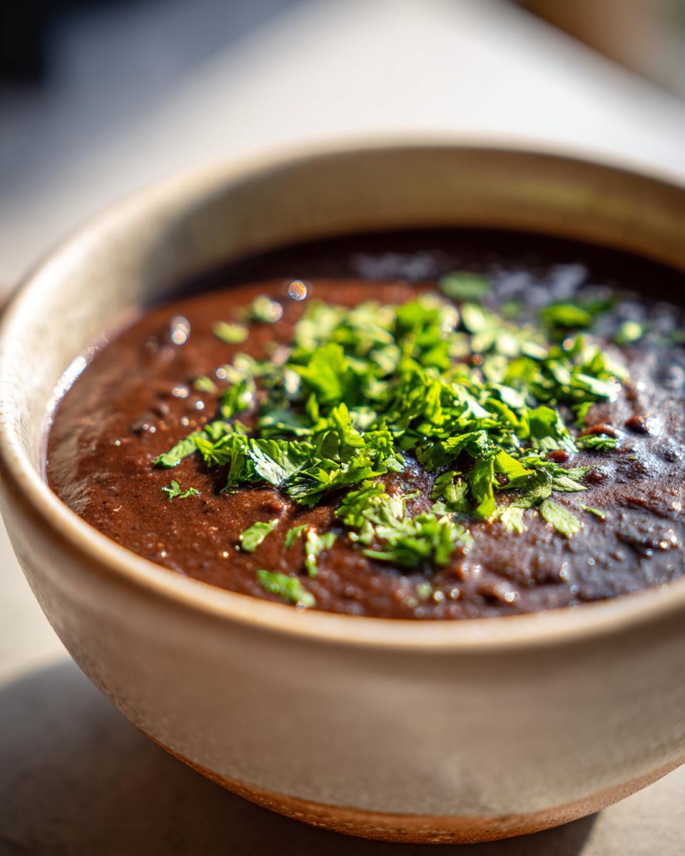 Close-up of a bowl of rich, creamy black bean soup topped generously with fresh chopped cilantro or parsley.