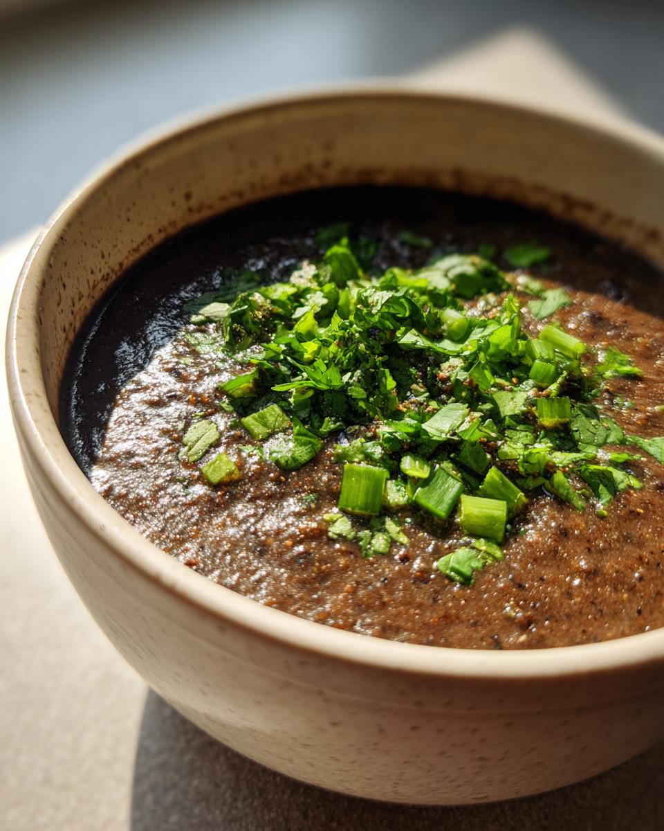Close-up of a bowl of creamy black bean soup garnished generously with chopped fresh cilantro and green onions.