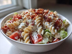Close-up of a bowl filled with creamy blt pasta salad featuring rotini pasta, lettuce, tomatoes, and crispy bacon bits.