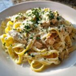 A close-up of creamy chicken alfredo pasta topped with grated parmesan and fresh chopped parsley.