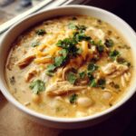 Close-up of a creamy white chicken chili recipe bowl topped with shredded cheese and fresh cilantro.