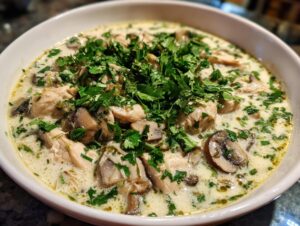 Close-up of creamy coconut soup with chunks of chicken, sliced mushrooms, and fresh parsley.