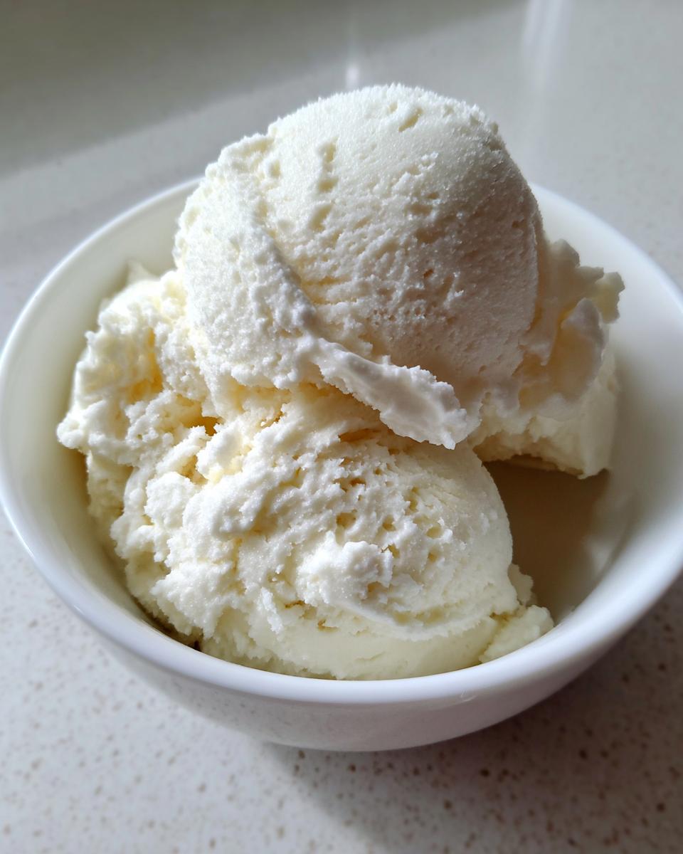 Close-up of three scoops of creamy white cottage cheese ice cream served in a small white bowl.