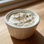 A small white ramekin filled with creamy horseradish sauce for prime rib, topped with spices.
