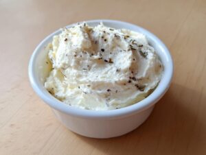 A small white bowl filled with creamy, whipped horseradish sauce for prime rib, topped with herbs and pepper.