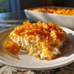 A generous serving of creamy hot chicken salad topped with melted cheese and crunchy cornflakes on a white plate.