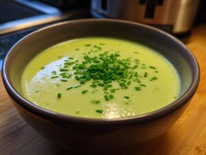 Close-up of a bowl of creamy, light green leek soup topped generously with fresh chopped chives.
